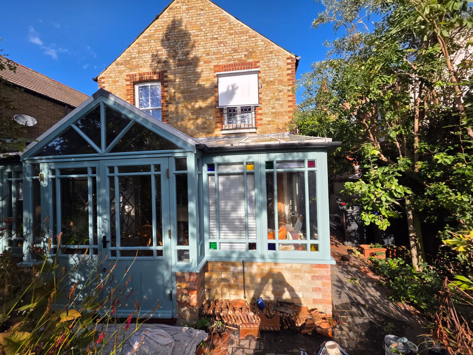 Timber conservatory finished in sage green, with the house's windows in white